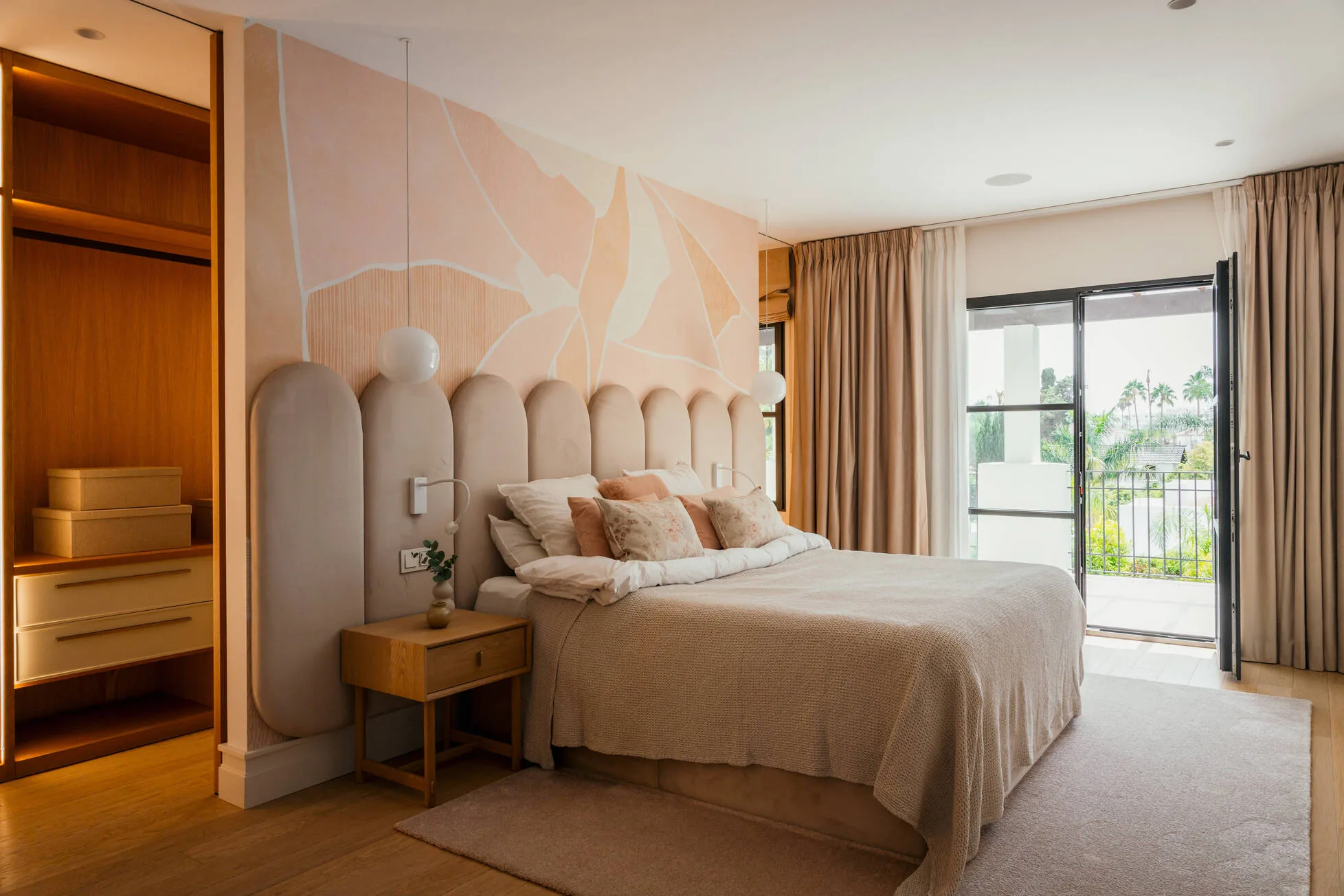 A bedroom in blush plaster with a hand-painted mural and arched headboard