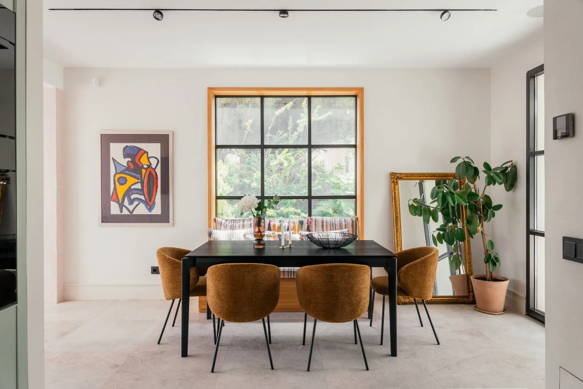 The dining table beneath track lighting, a tall oak-framed window onto the garden