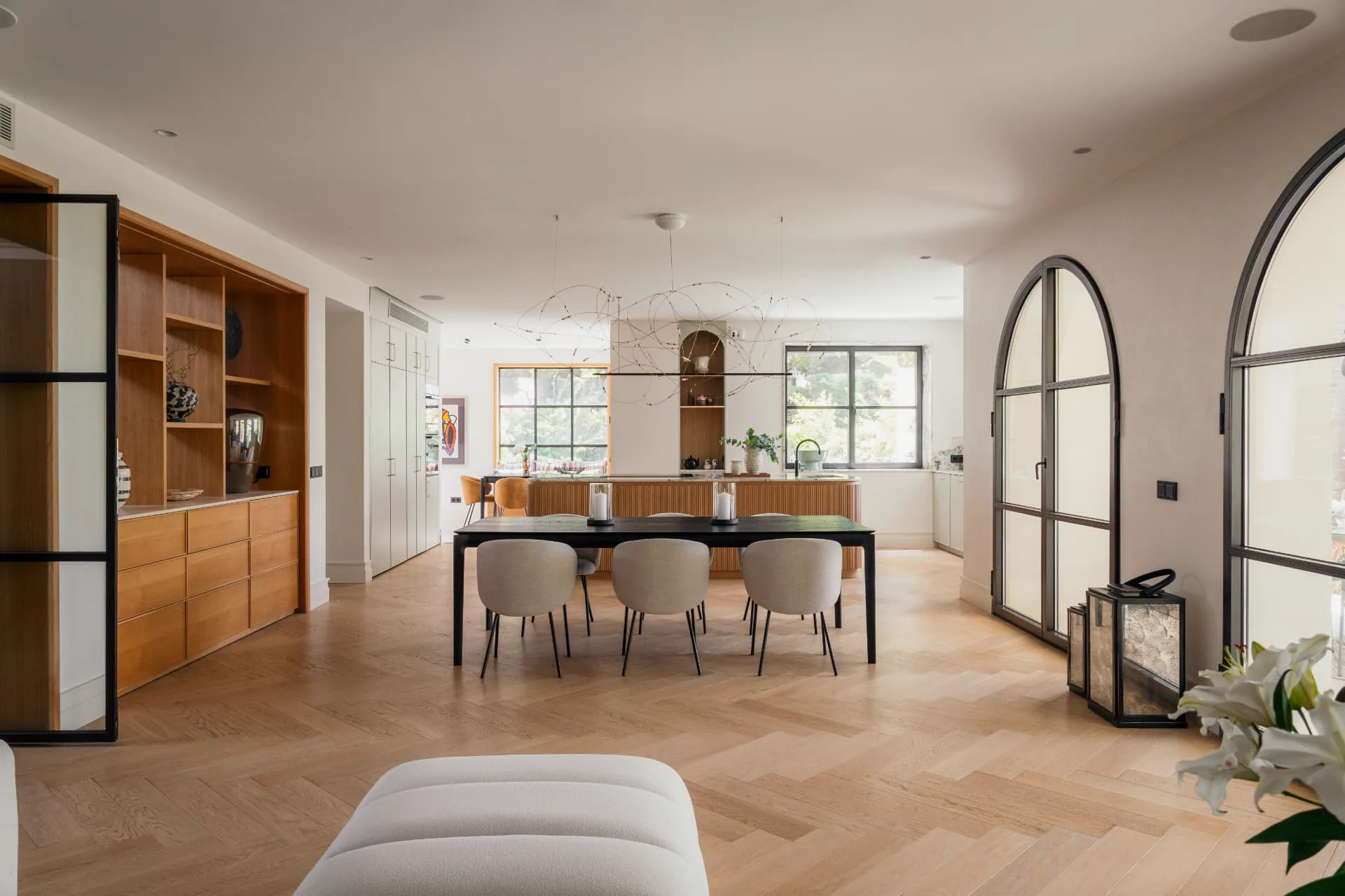 The dining table set beneath a wire chandelier, arched doors to the garden