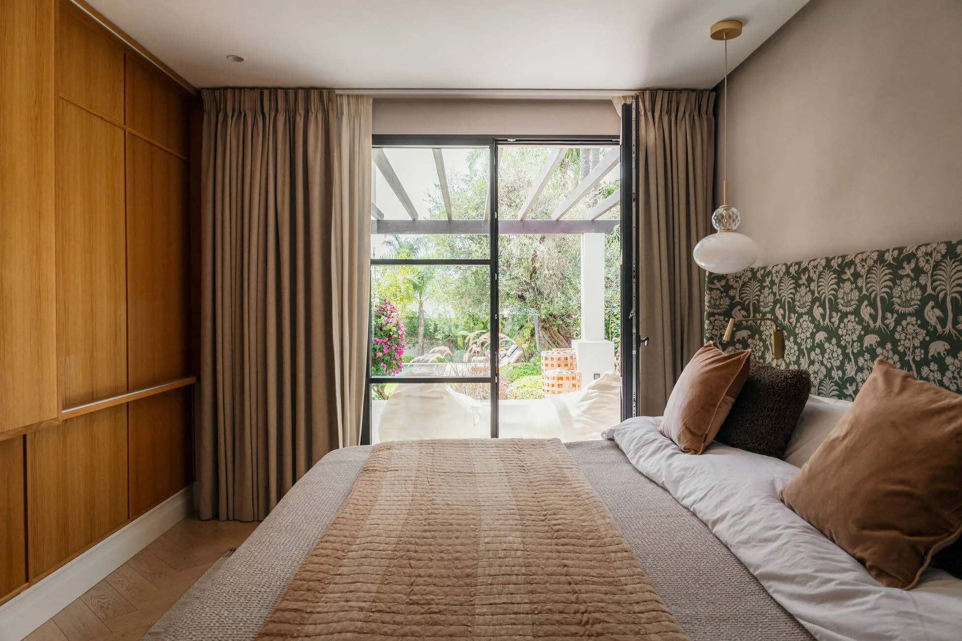 A bedroom opening onto the garden, green patterned headboard and oak joinery