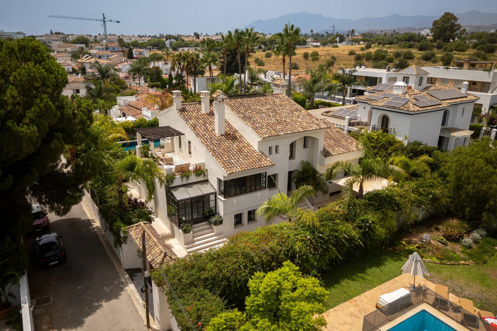 La Serena from above: tiled roofs, pergola and pool amid palms, the sierra beyond