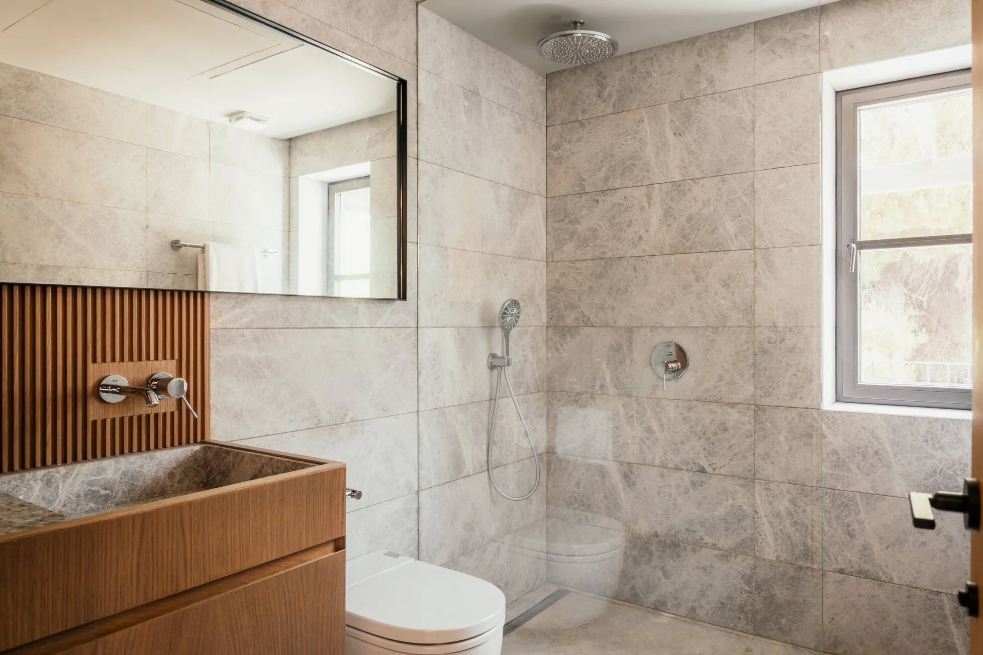 A guest bathroom in pale stone with an oak vanity and walk-in rain shower