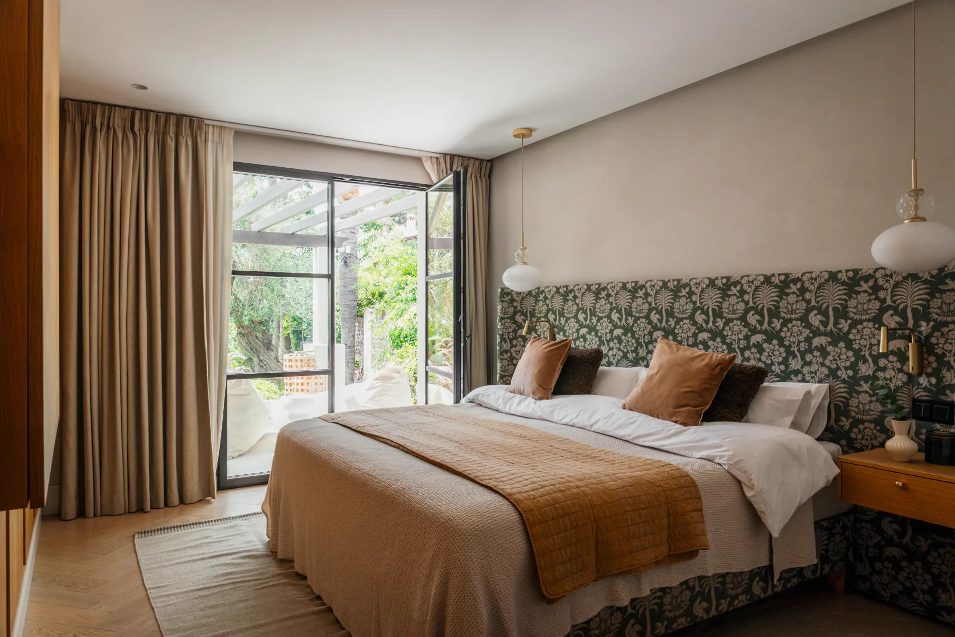 A guest bedroom with patterned green headboard and doors open to the terrace