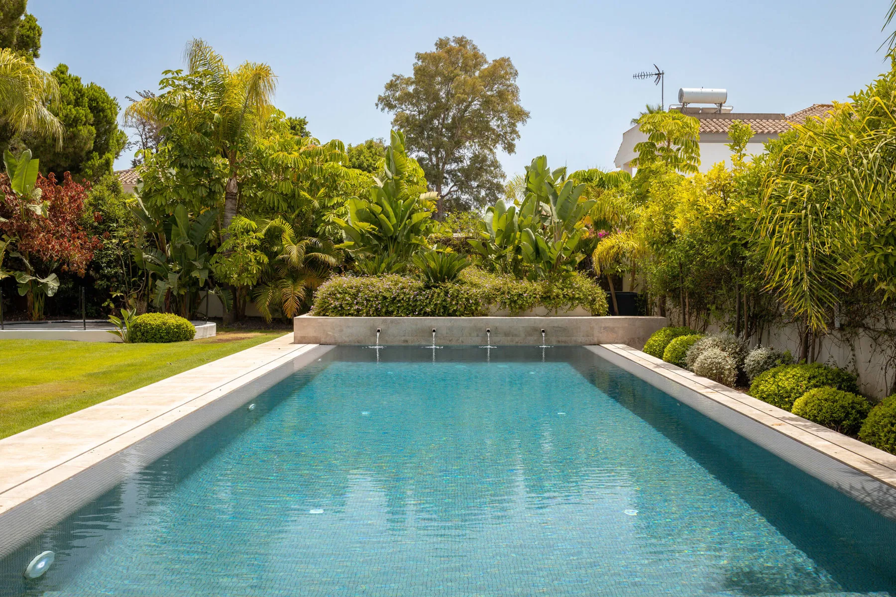 The mosaic-tiled pool with four stone water spouts, framed by tropical planting