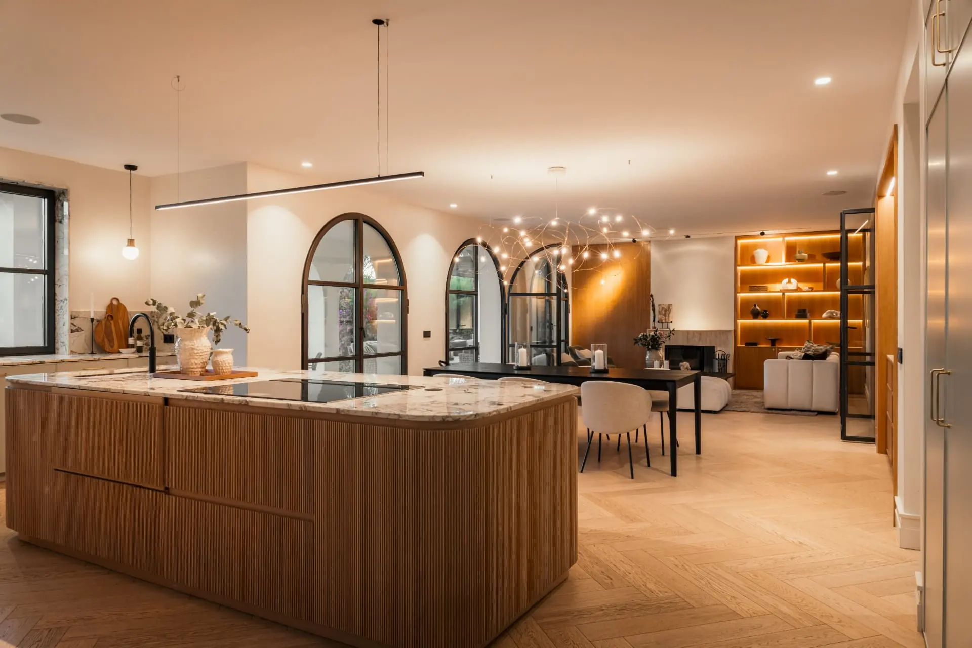The kitchen island and dining room at night, arched doors and lit oak shelving