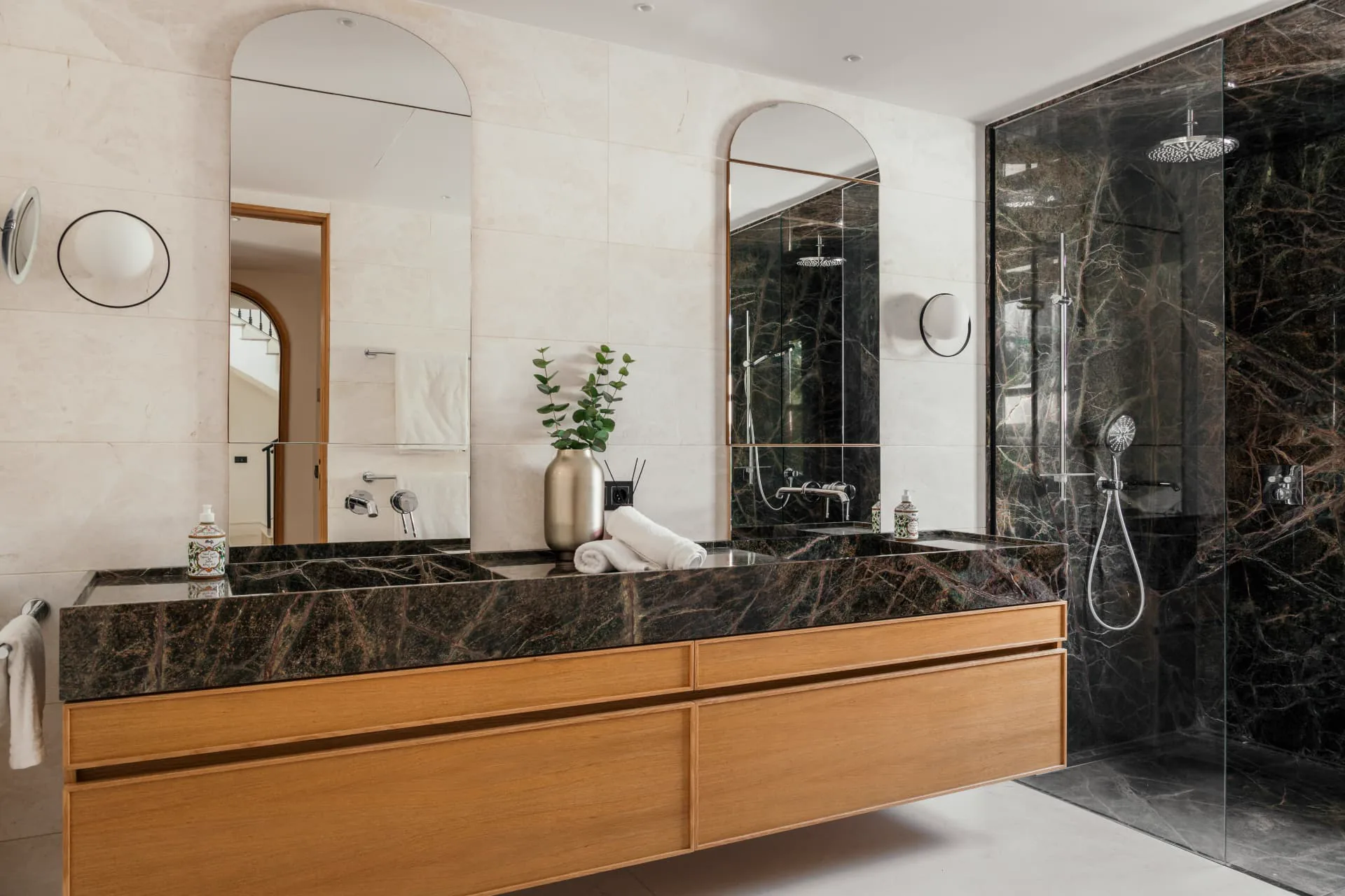 A bathroom in cream stone and dark veined marble with a floating oak vanity